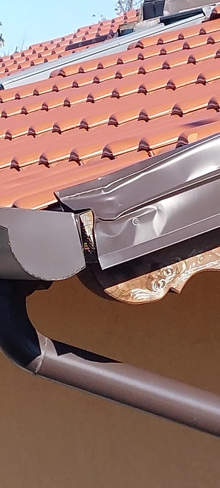 Verbogene Metall-Dachrinne, die potenzielle Probleme bei der Wasserableitung auf dem gefliesten Dach verursacht.