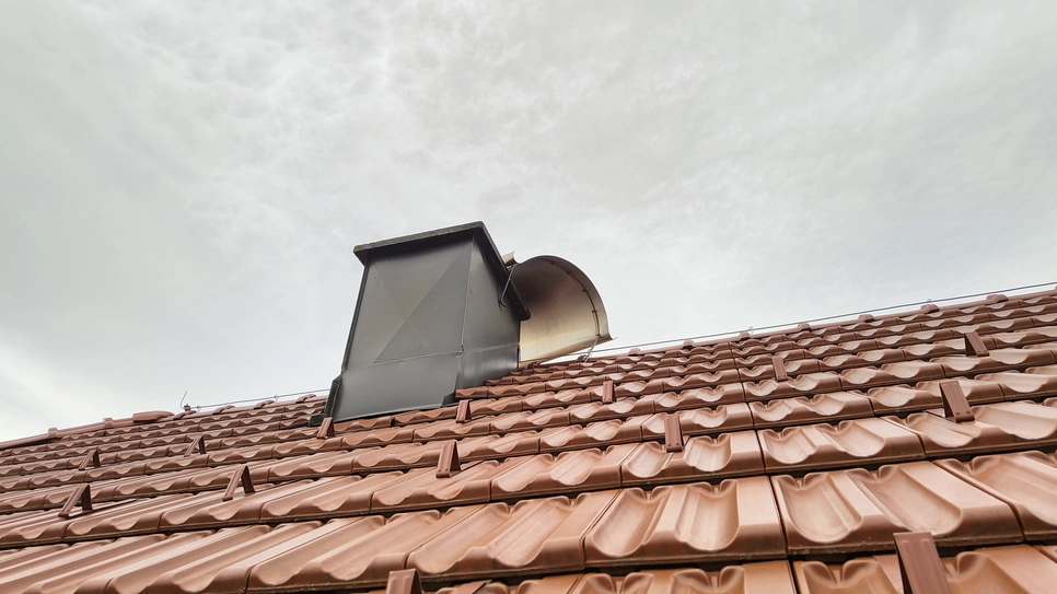 Schornsteinstruktur, die in ein braunes keramisch gefliestes Dach unter einem bewölkten Himmel integriert ist.