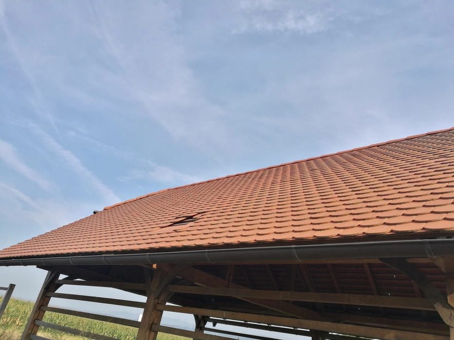 Gebrochener Dachziegel auf einer Holzstruktur, der eine Lücke in der gefliesten Oberfläche gegen einen klaren Himmel schafft.