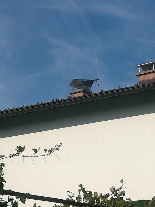 Schornstein mit Schutzhaube auf einem Wohnhausdach gegen den klaren Himmel, der die Belüftung gewährleistet.