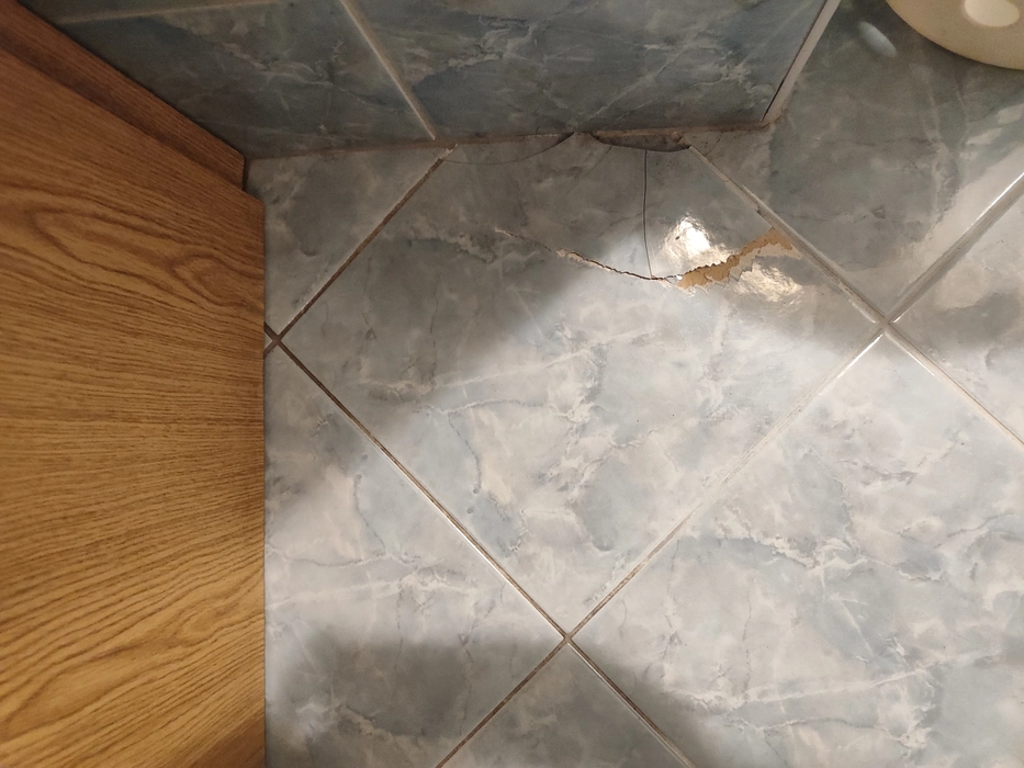 Badezimmerfliese mit sichtbarem Riss und Schäden in der Nähe der Ecken, die eine Verschlechterung zeigen.