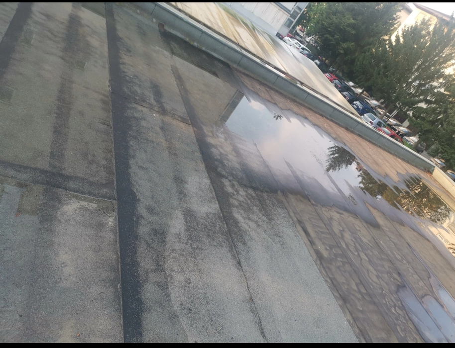 Flachdach mit sichtbaren Wasseransammlungen, die auf mögliche Entwässerungsprobleme oder Oberflächenschäden hinweisen.