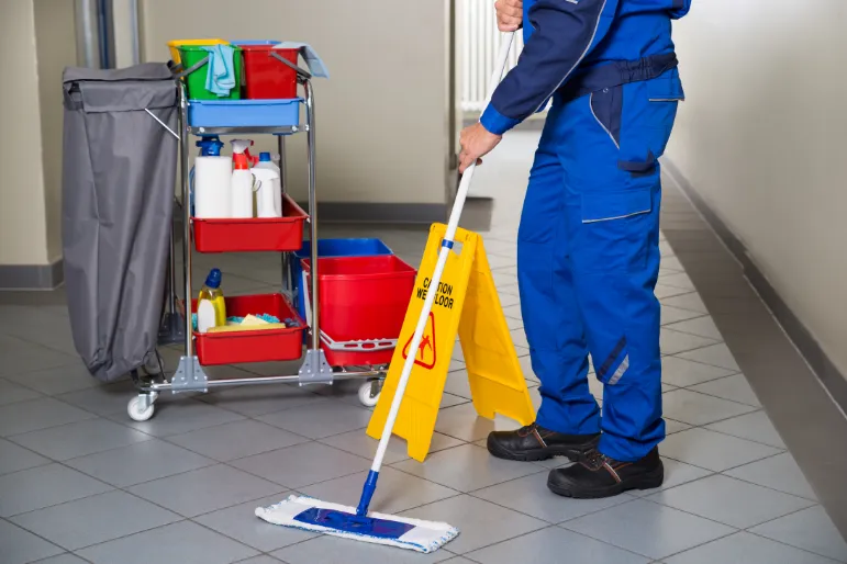 Bodenreinigung im wc Ein Reiniger wischt mit einem feuchten Mopp die Fliesen auf dem Boden des Flurs, der zur Toilette führt.