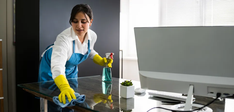 Reinigung des schreibtisches Die Reinigungskraft wischt den Schreibtisch mit dem Computer-Monitor ab.