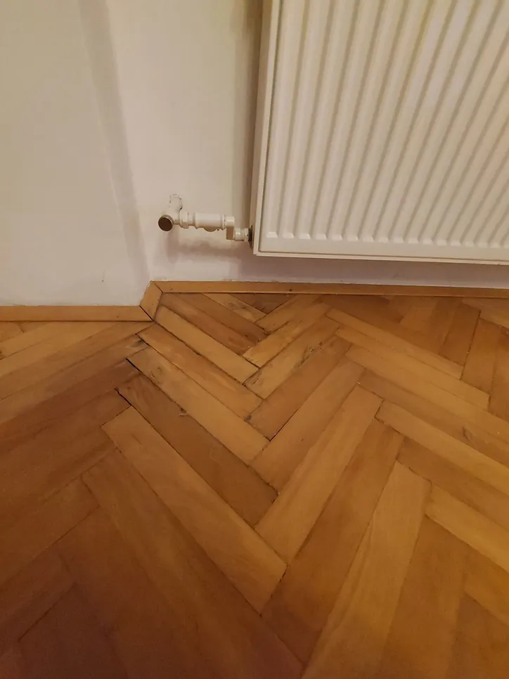 Wassergeschädigter Parkettboden neben einem wandmontierten Heizkörper deutet auf mögliche Undichtigkeiten hin.